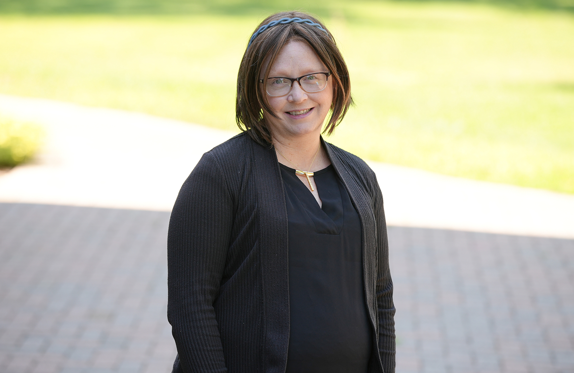 A women with shoulder length brown hair wairing glasses and sweater and shirt, smiling at the camera. 