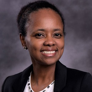 Image of Jenean Castillo, a smiling black woman with black hair pulled back, she is wearing a jacket and blouse.