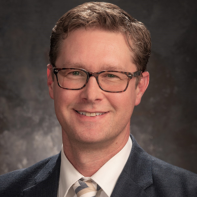 Image of Eric Moody, a white man with brown hair and glasses, they are wearing a oxford shirt and smiling at the camera.