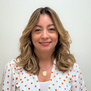 Carol Salas Pagán, a Latina with long brown hair wearing a white shirt with red dots 