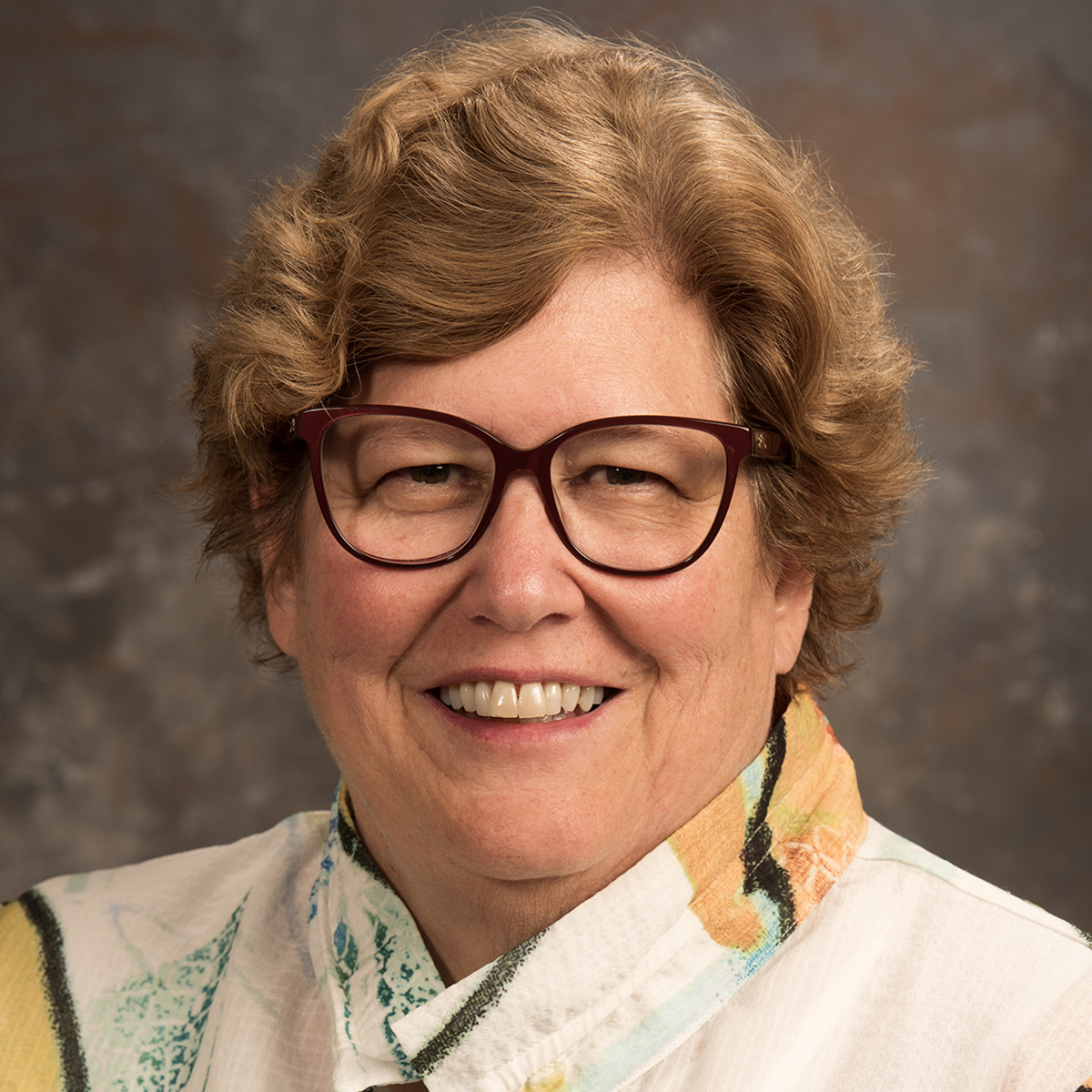 Sandy Root-Elledge, a smiling woman with glasses and short hair.