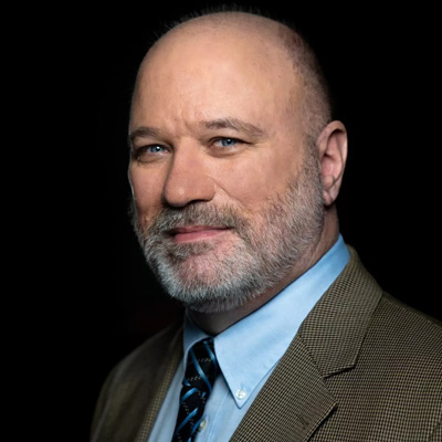 Image of Andrew Houtenville, a white male with greying hair and bear, he is wearing a suit with a tie.